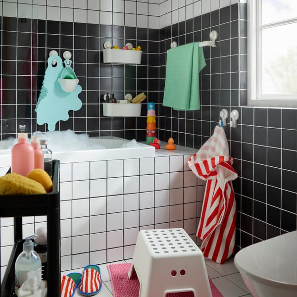 A small family bathroom in black-and-white tiles. Plenty of TISKEN hooks and baskets with suction cups around the bathtub.