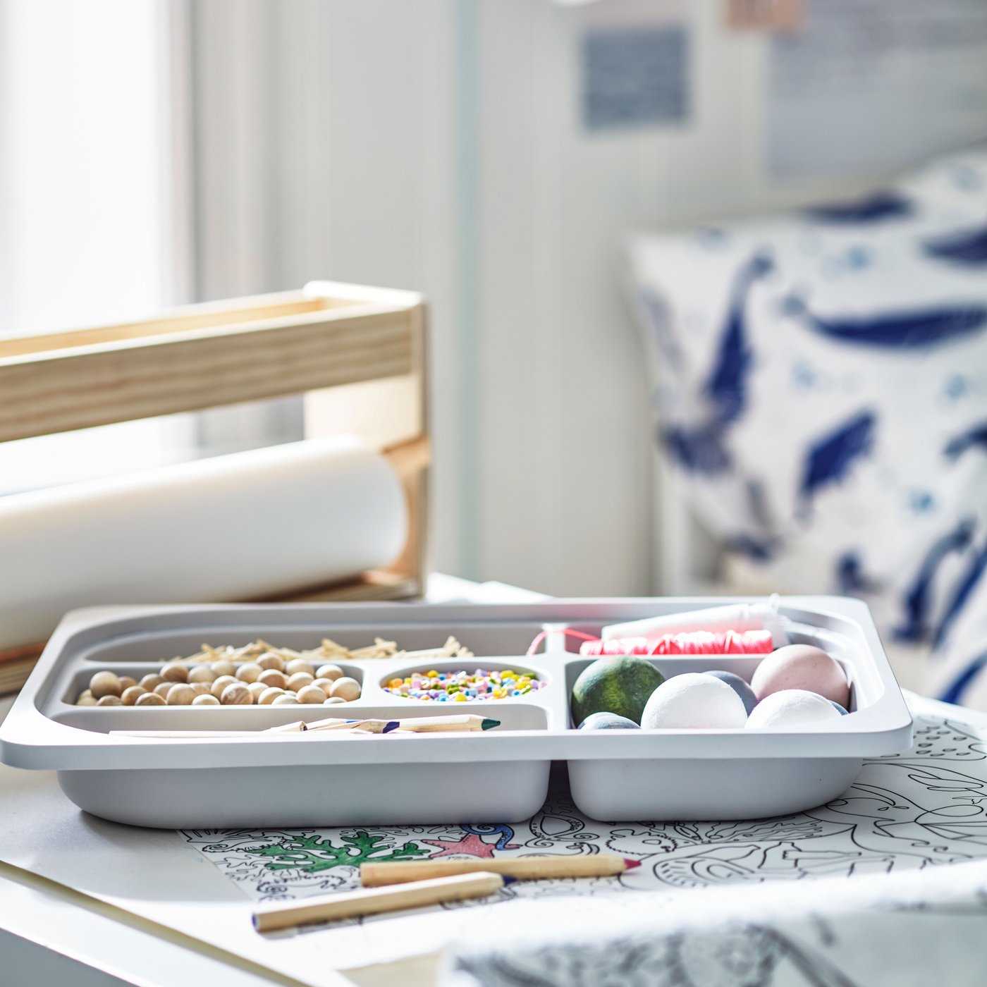 מגש אחסון TROFAST עם תאים מונח על גבי נייר מגליל נייר צביעה של BLÅVINGAD.