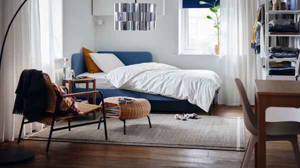 Un dormitorio con una estructura de cama tapizada con cabecero de esquina, funda de edredón y funda de almohada blancas y una planta en maceta, todo de IKEA.