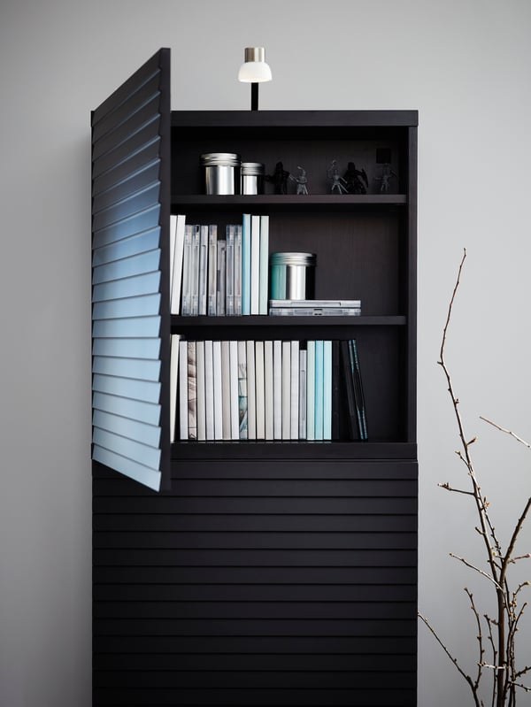 A cabinet with accent slatted doors in anthracite and a nickel-plated LED lamp on top, door is open, books are inside.