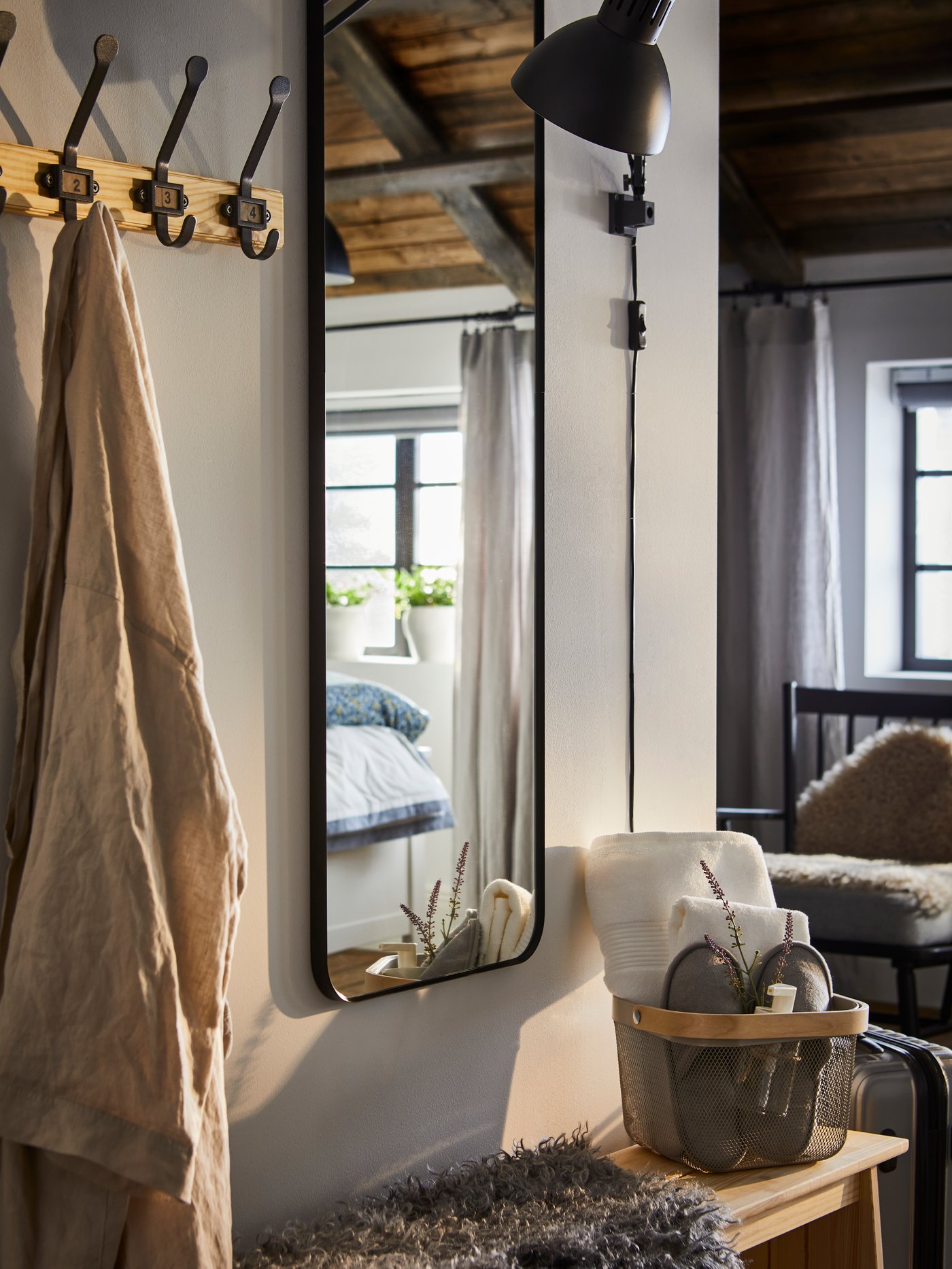 A KARTOTEK rack with 5 hooks and a black LINDBYN mirror are attached to a wall near a stool with a basket on top.