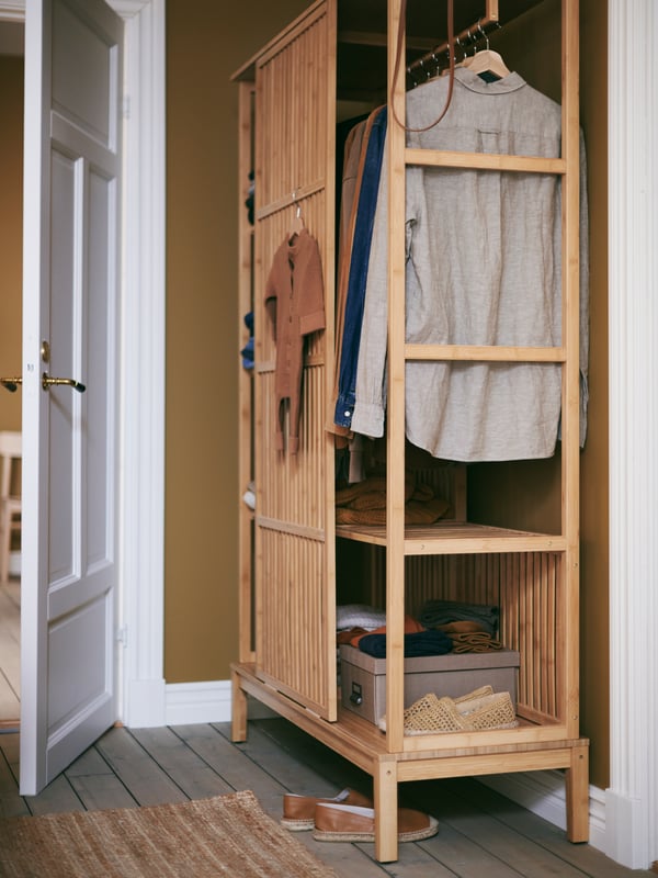 A compact NORDKISA wardrobe, beside an open white door, houses a small collection of clothes on hangers plus shoes and boxes.