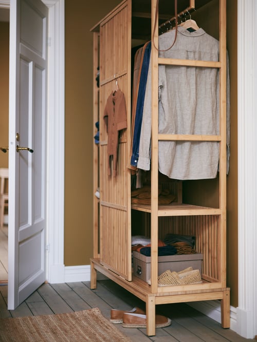 In einem kompakten NORDKISA Kleiderschrank neben einer offenen weißen Tür sind Kleidungsstücke auf Kleiderbügeln sowie Schuhe und Boxen zu sehen.