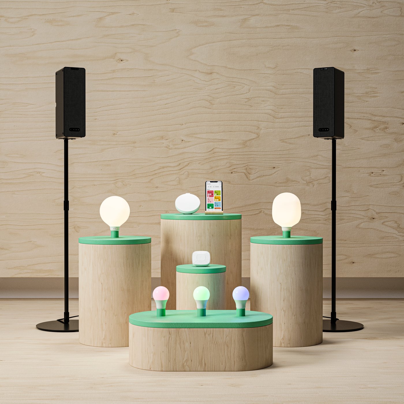 Fem träpodier i olika storlekar och höjder med gröna ovansidor, var och en med olika smarta glödlampor i varierande storlek och färg. Vissa lampor lyser med vitt ljus, andra med färgat ljus. Två svarta högtalare på stativ står symmetriskt i bakgrunden. En smartphone ligger på det högsta podiet i mitten med DIRIGERA app på skärmen. 