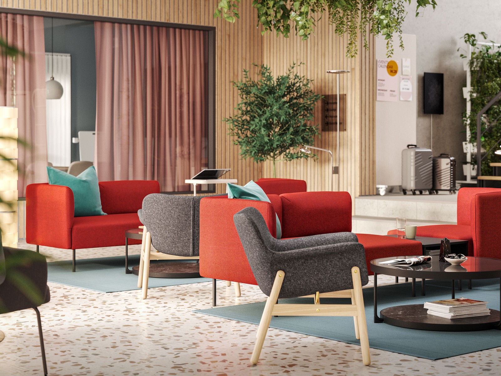 Seating groups with dark grey VEDBO armchairs and red modular sofas are in the middle of a light-filled, modern hotel lounge.