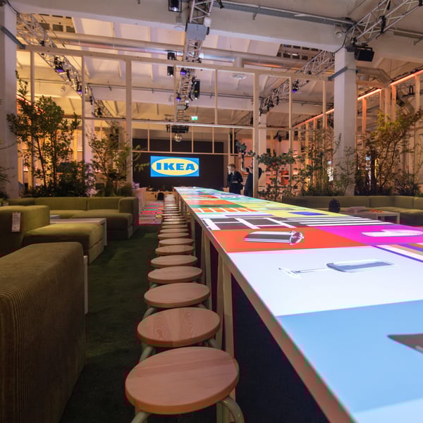 Dettaglio dell'interno della location del fuorisalone 2025 con un tavolo illuminato da un proiettore con loghi colorati.