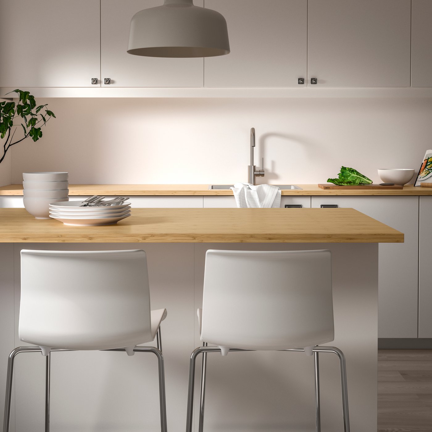 A kitchen with HOLMARED custom-made worktop in bamboo/veneer on the kitchen island, tableware, and two white kitchen chairs. 
