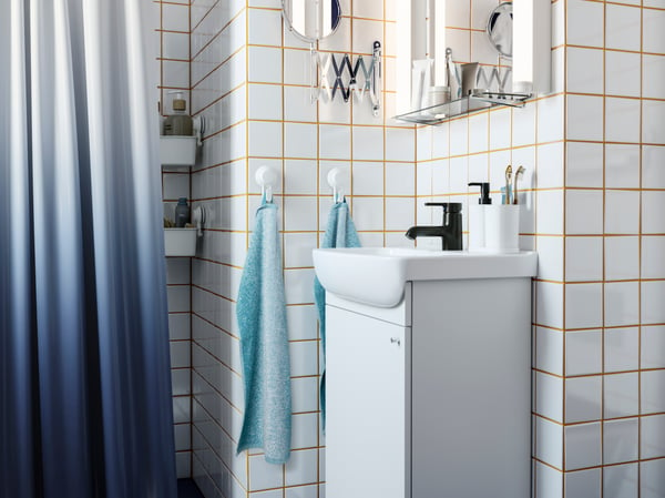 A white wash-basin cabinet, a black tap, white tiles with yellow grout, a dark blue shower curtain, hooks with towels.