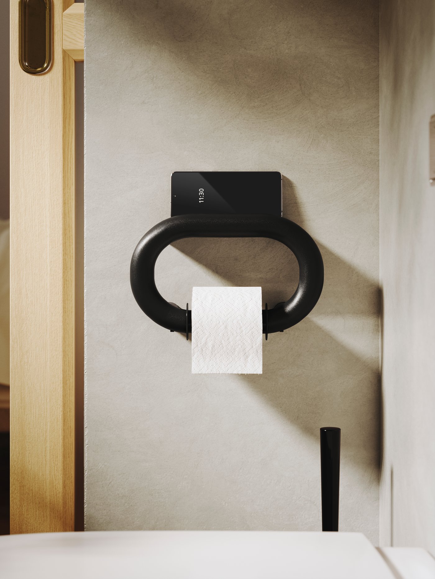 A BÄSINGEN toilet roll holder in anthracite is mounted on a bathroom wall in soft beige and it has a toilet paper roll on it.