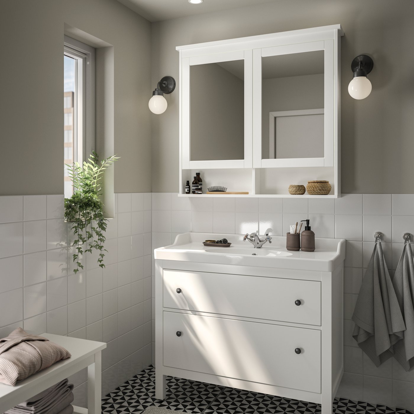A grey bathroom with a big window has a white HEMNES washstand, a black RÅSKOG trolley and a MOSSJÖN glass door cabinet.