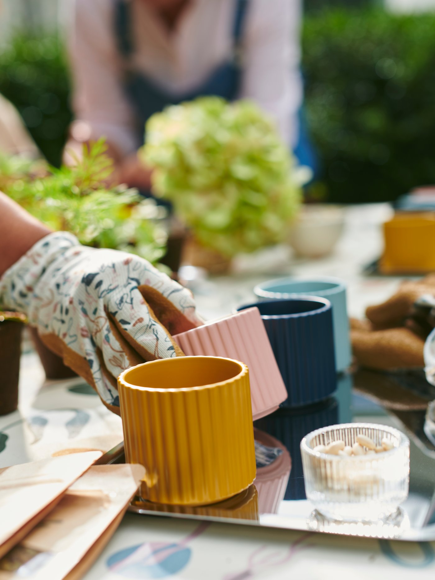 En person håller på att plantera i små färgglada krukor utomhus.