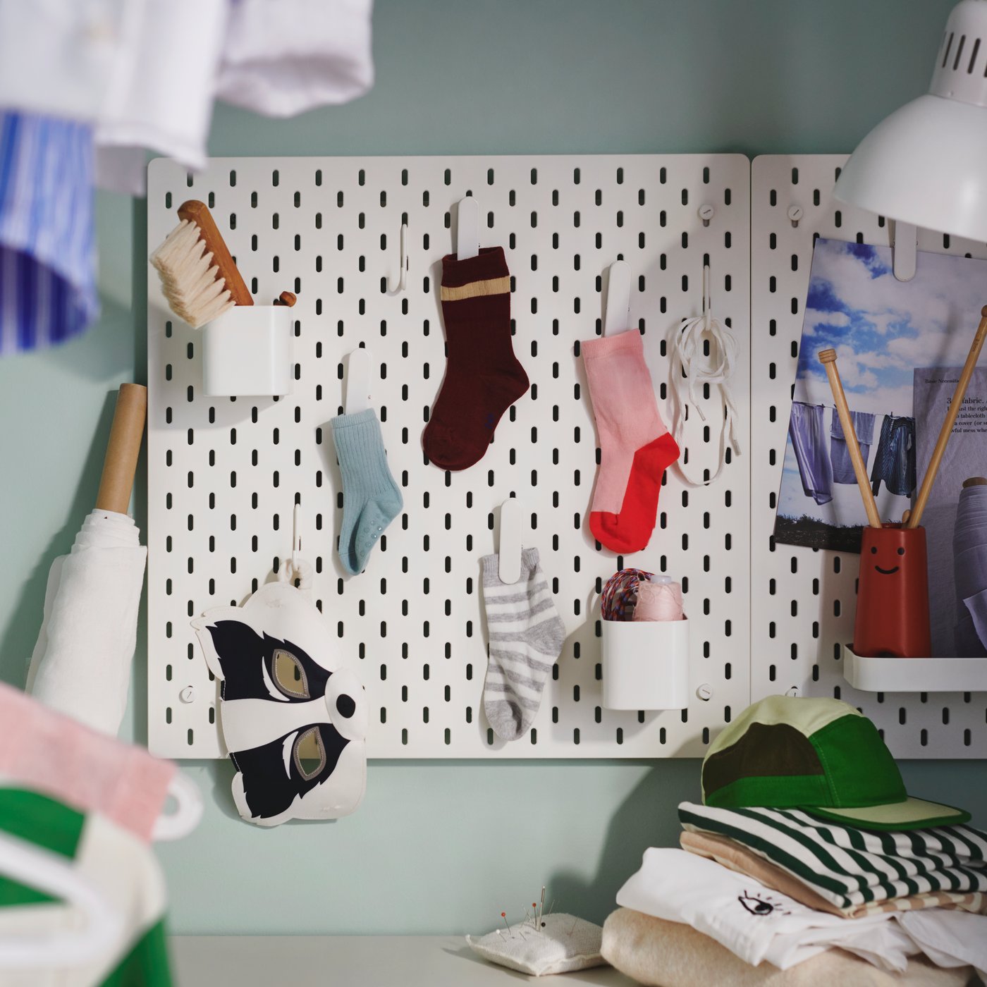 Two square, white SKÅDIS pegboards are on a laundry room wall, holding single socks in clips and thread spools in containers.