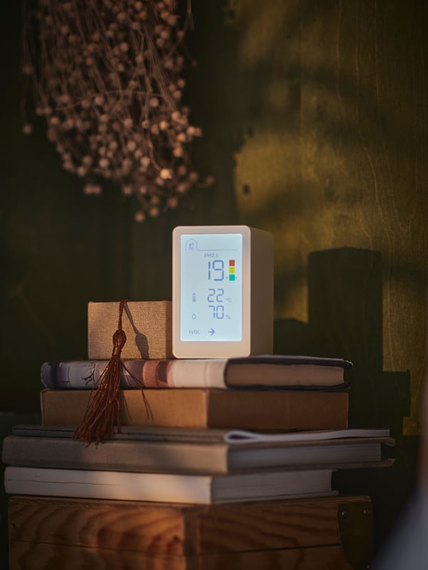 VINDSTYRKA air quality sensor with LED screen showing different air quality readings on a stack of books in the home.