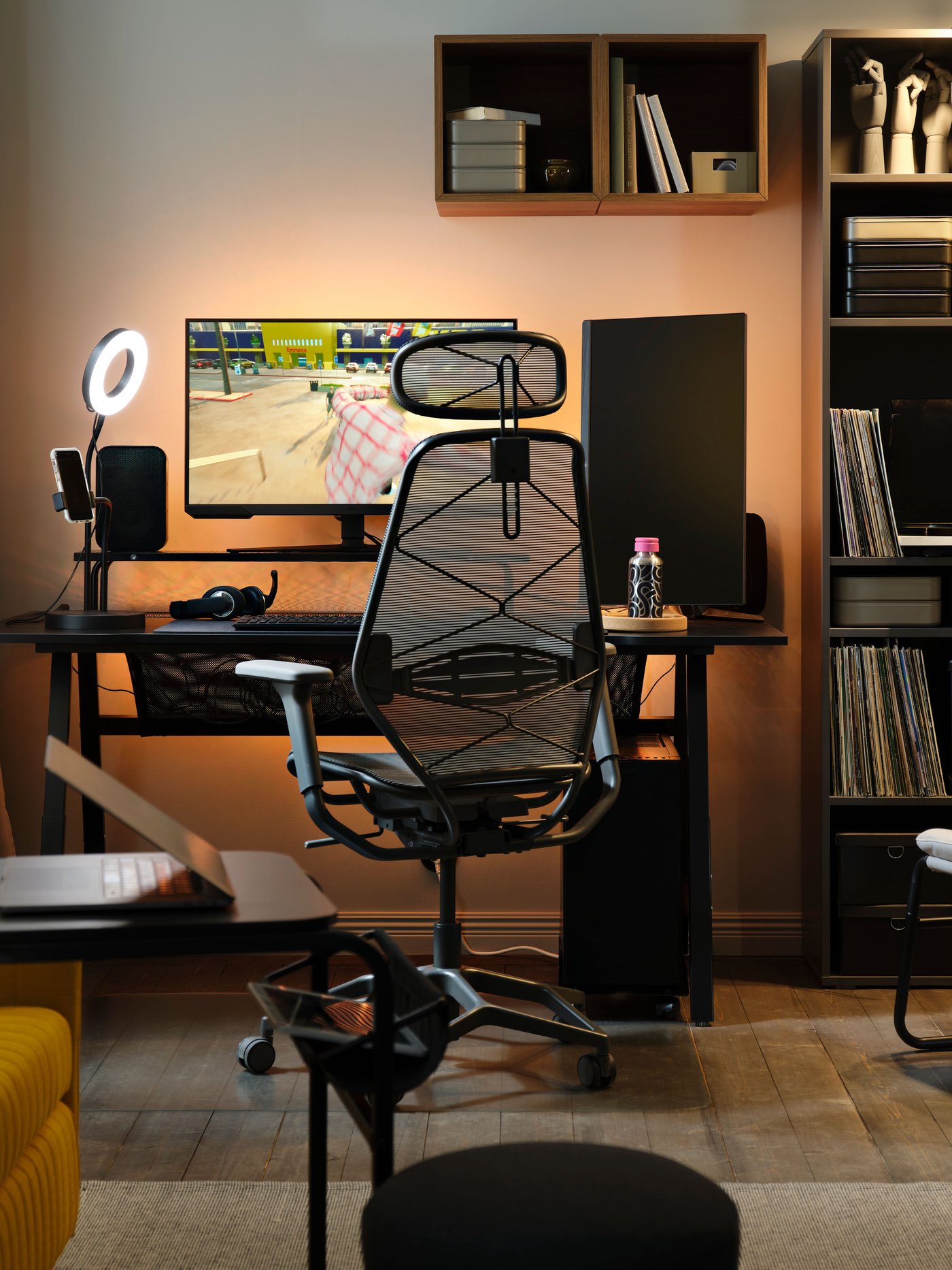 Un espai gaming retroil·luminat amb un ordinador; hi ha un escriptori gaming UTESPELARE negre amb un monitor on es mostra una partida en pausa i, al costat, una cadira de malla de color gris.