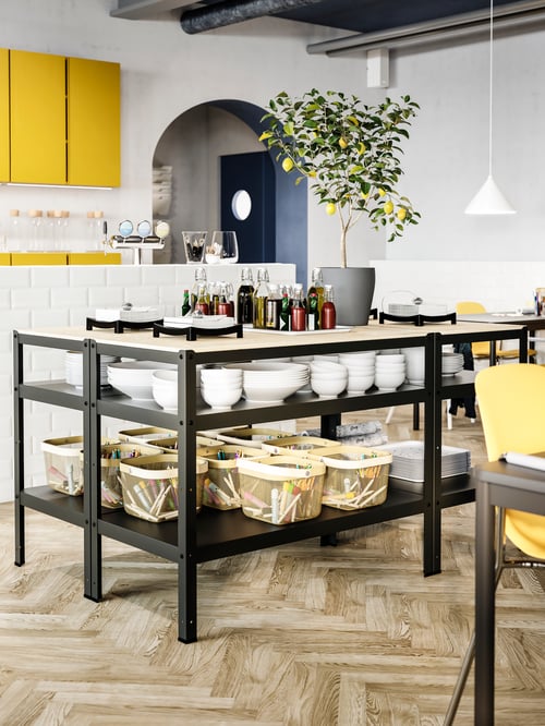 Dining room with multiple work benches containing white bowls, baskets and a potted plant., with a white pendant lamp above.