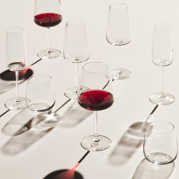 DYRGRIP red wine glasses are placed on a white surface. They are lit from behind and cast shadows in an eye-catching way.