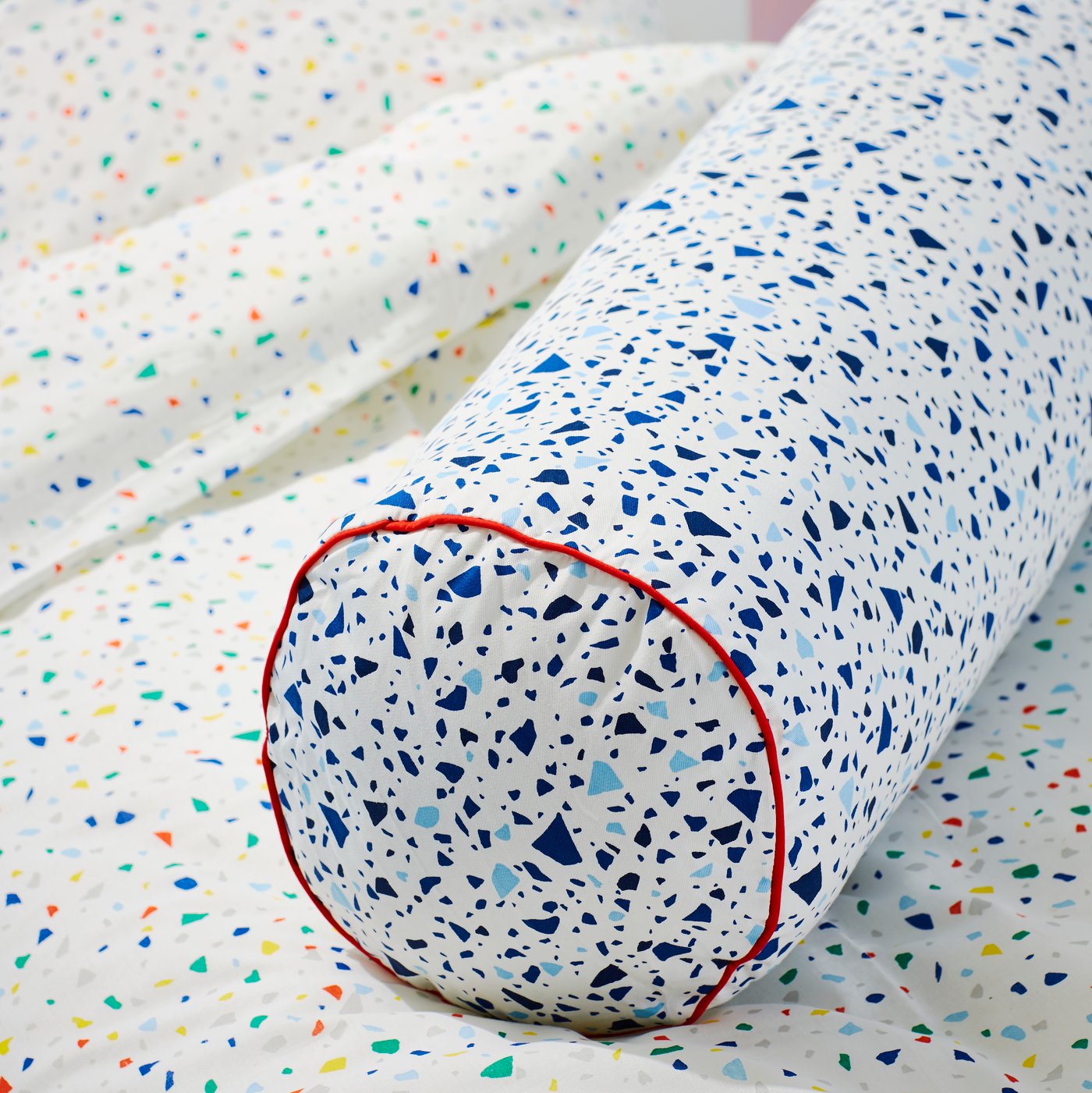A MÖJLIGHET cushion with a pattern of blue dots lies on top of a duvet inside a MÖJLIGHET duvet cover with a mosaic pattern.