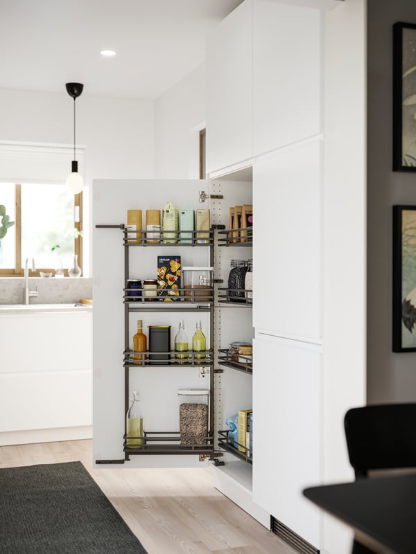 A kitchen with matte white VOXTORP fronts has a UTRUSTA pull-out larder with food packages and containers stored inside.