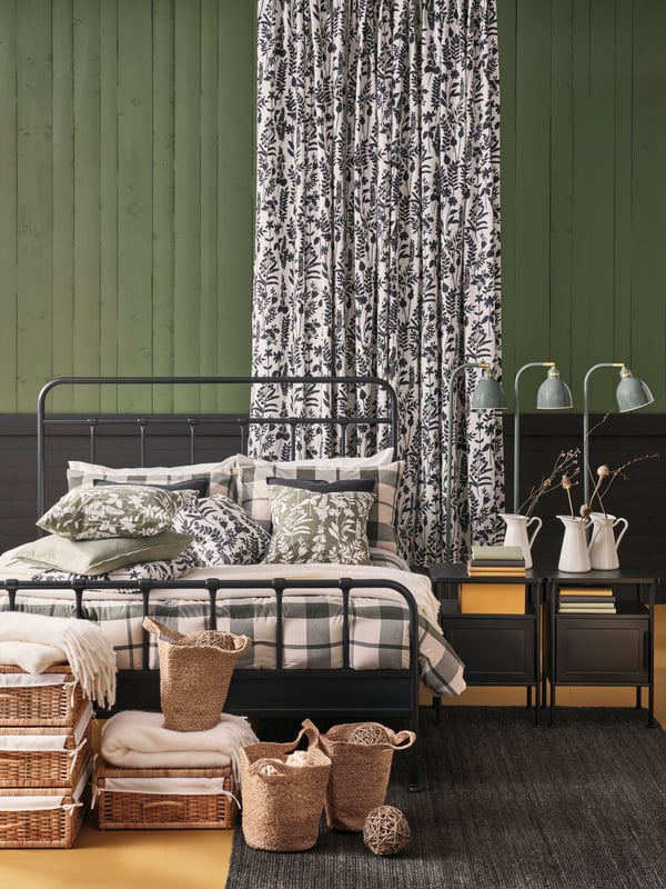 An anthracite STJÄRNÖ bed dressed with BESKSÖTEMAL 3-piece comforter set. Rattan boxes and jute bags stand in front.