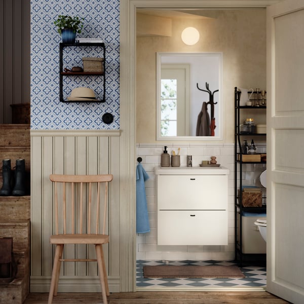 Un moble de bany ENHET/TVÄLLEN blanc amb lavabo i amb calaixos col·locat contra una paret amb rajoles d'estil retro en un bany tradicional situat sota una escala.