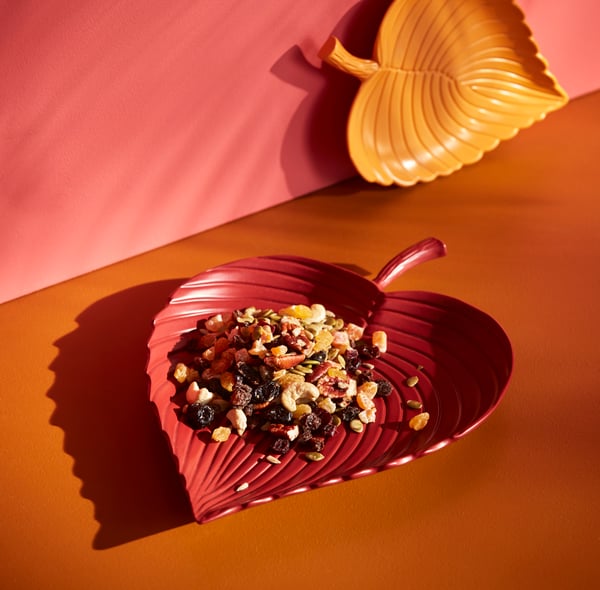 A red tray in the shape of a leaf with trail mix displayed.