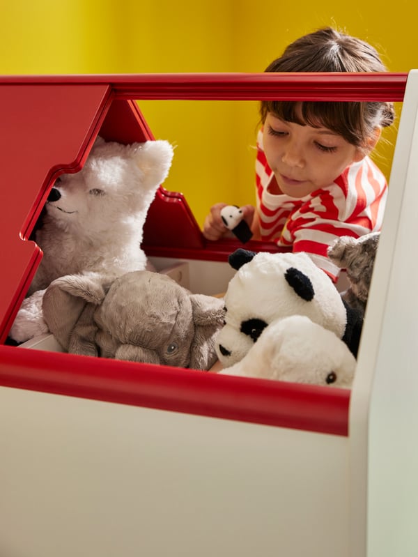 Close-up of VITBJÖRN storage unit with drawer, full of soft toys and a with a girl looking into it through the open top.