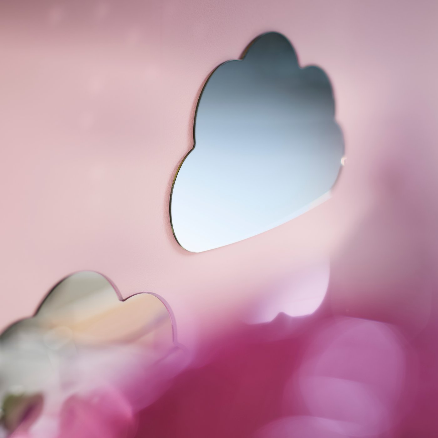 HOLMÖARNA mirror in a cloud shape mounted on a pink wall above a bed with colourful bedding in a children’s bedroom.
