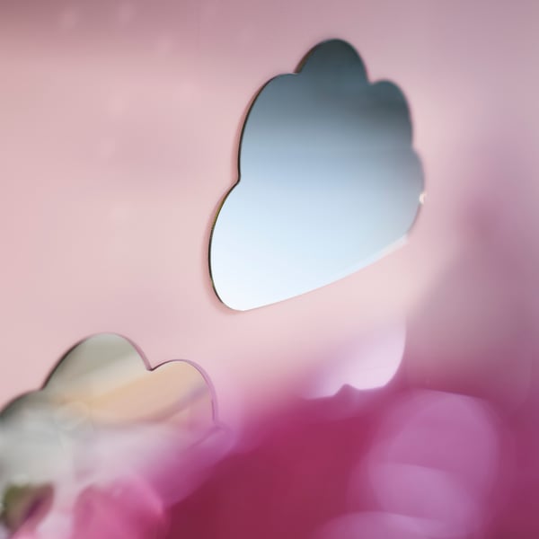 Miroir HOLMÖARNA en forme de nuage monté sur un mur rose au-dessus d'un lit avec des draps colorés dans une chambre d'enfant.