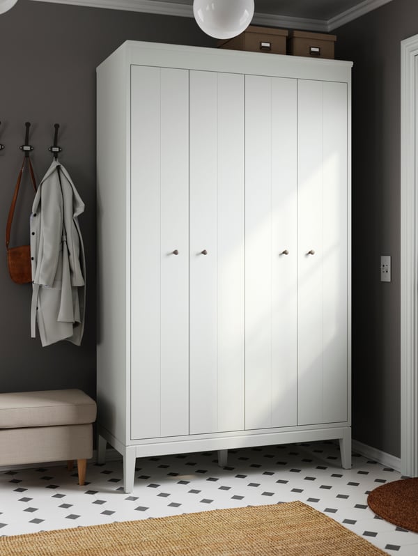 In a hallway with a black-and-white floor-tile pattern stands a white IDANÄS wardrobe. Stool by its side, thick rug below.