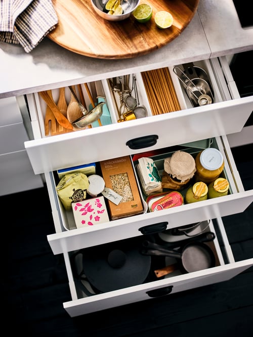 A kitchen featuring a cabinet with three opened drawers revealing a spoon, a fruit and herbal infusion tea and other items.