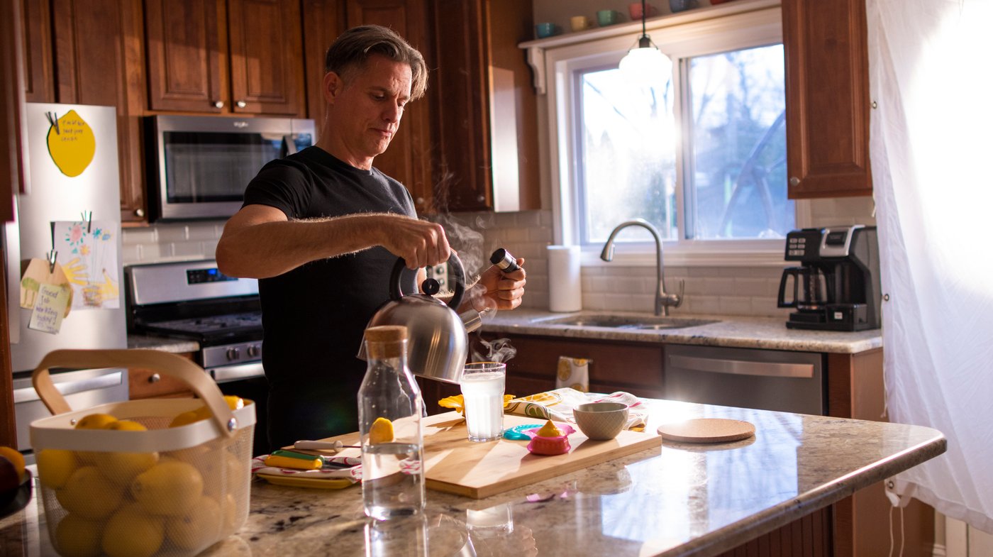 Man preparing a fresh lemon juice drink in a kitchen full of natural light.