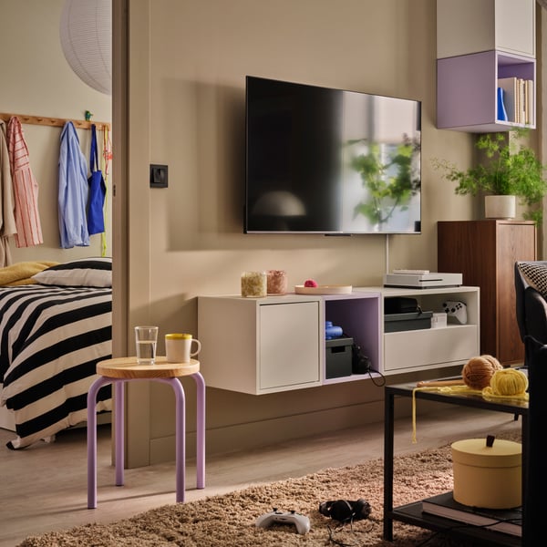 A light living room with a TV and a combination of EKET wall-mounted cabinets displaying books and decorative items.