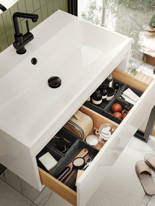 Overhead shot of an ÄNGSJÖN wash stand with one drawer open, revealing multiple boxes, and other items.