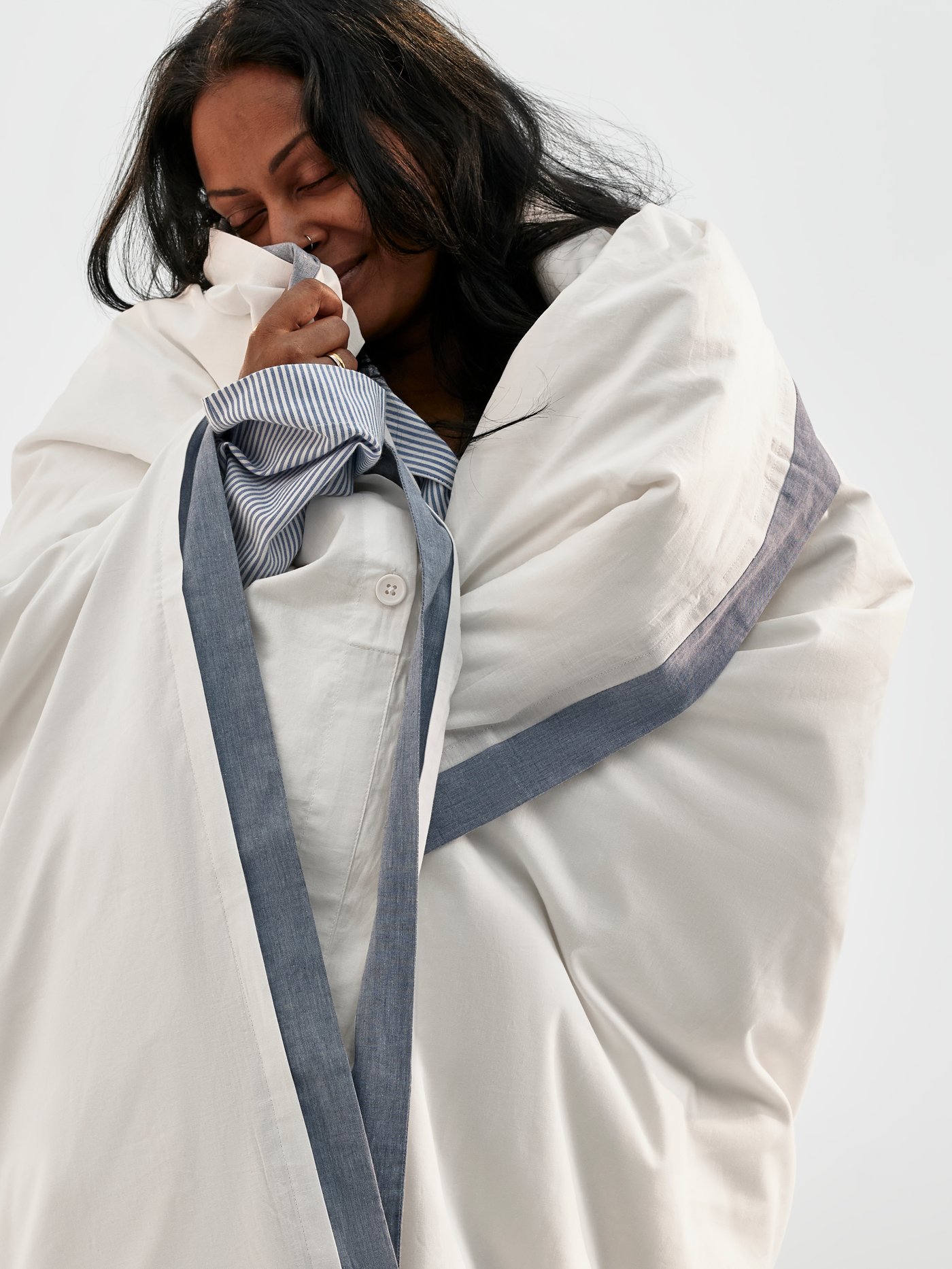 Someone standing and snuggling into a fluffy duvet that has a white cover made of 100% organic cotton.