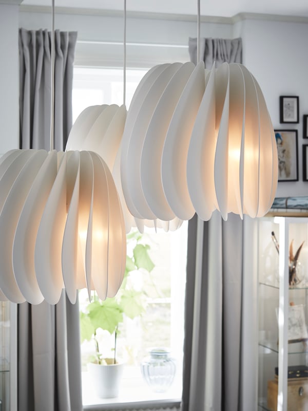 IKEA SKYMNINGEN white pendant lamps emitting soft light from a white slatted lampshade.