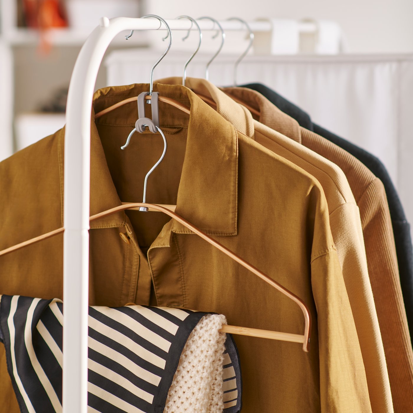 A close up of the end of a white RIGGA clothes rack with coats hanging on it and a scarf hanging on a OMTRENT hanger.