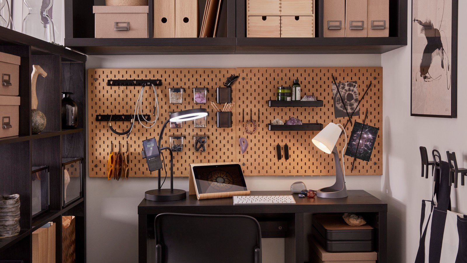 An organised workspace with a desk with work lamps and black-brown KALLAX shelving units and SKÅDIS pegboards on the wall.