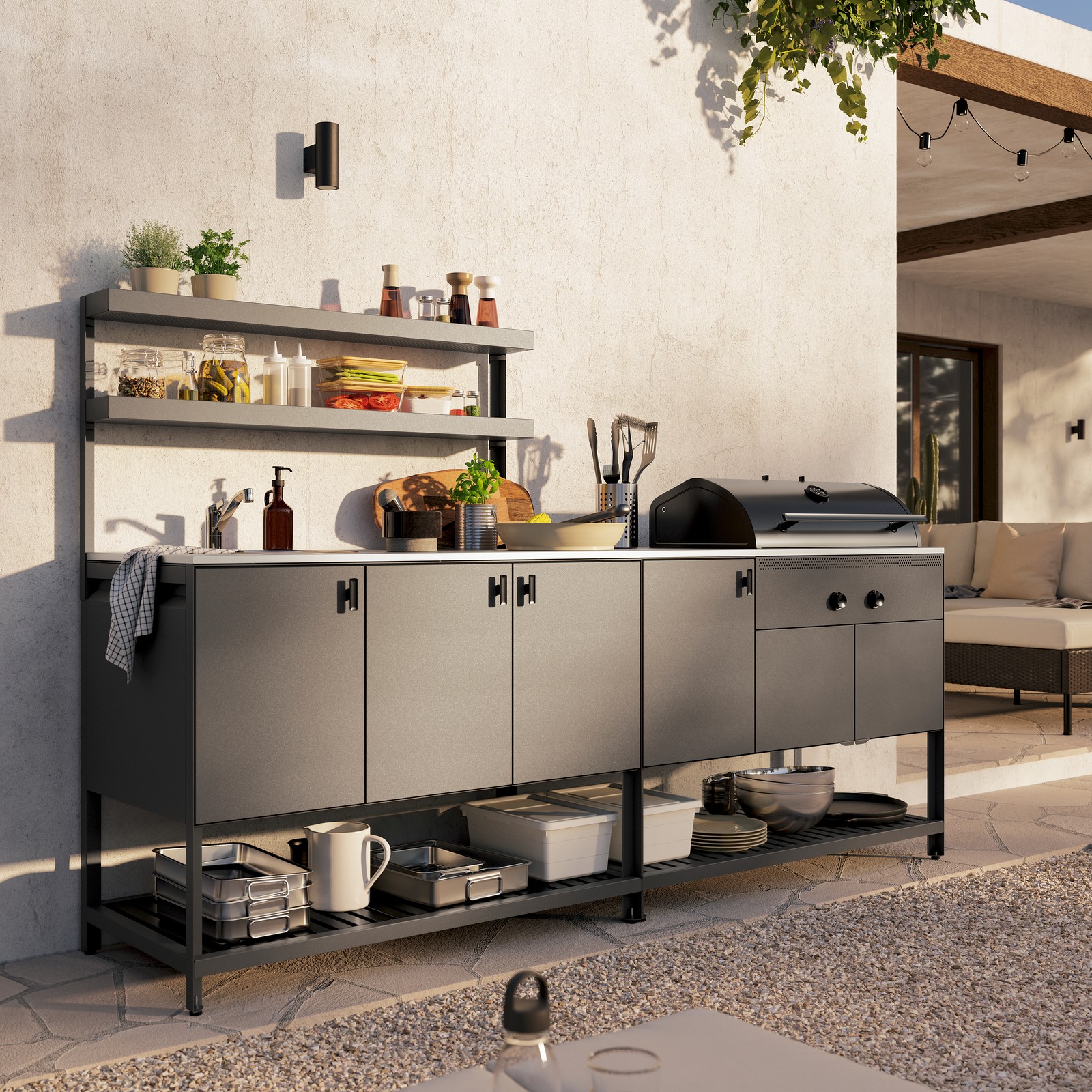 מטבח חיצוני אפור כהה מדגם BÅTSKÄR עם מנגל פחמים. מעל הארונות הסגורים שני מדפים פתוחים עם עשבי תיבול טריים.