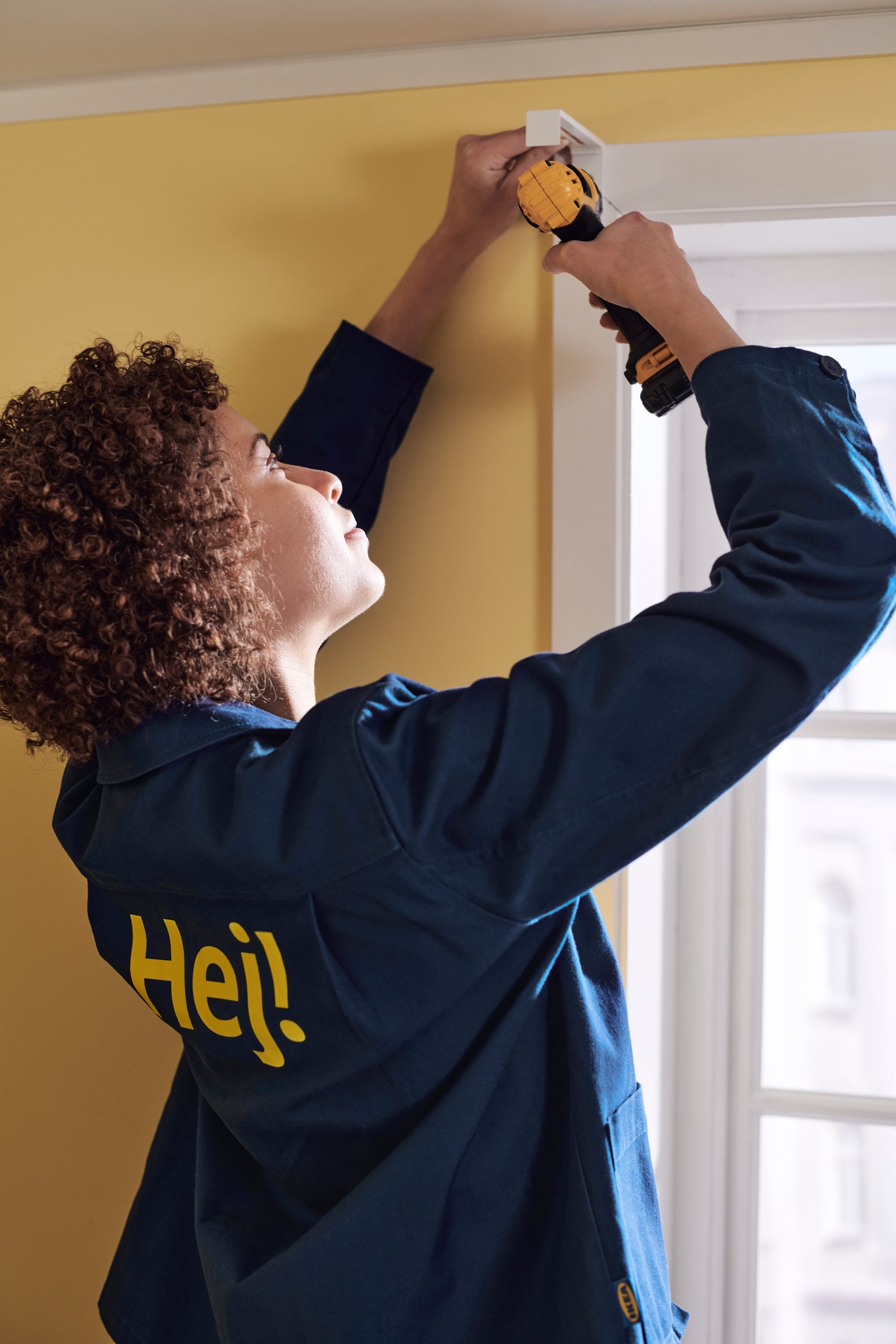 Ein IKEA MItarbeiter bohrt ein Loch in eine gelbe Wand.