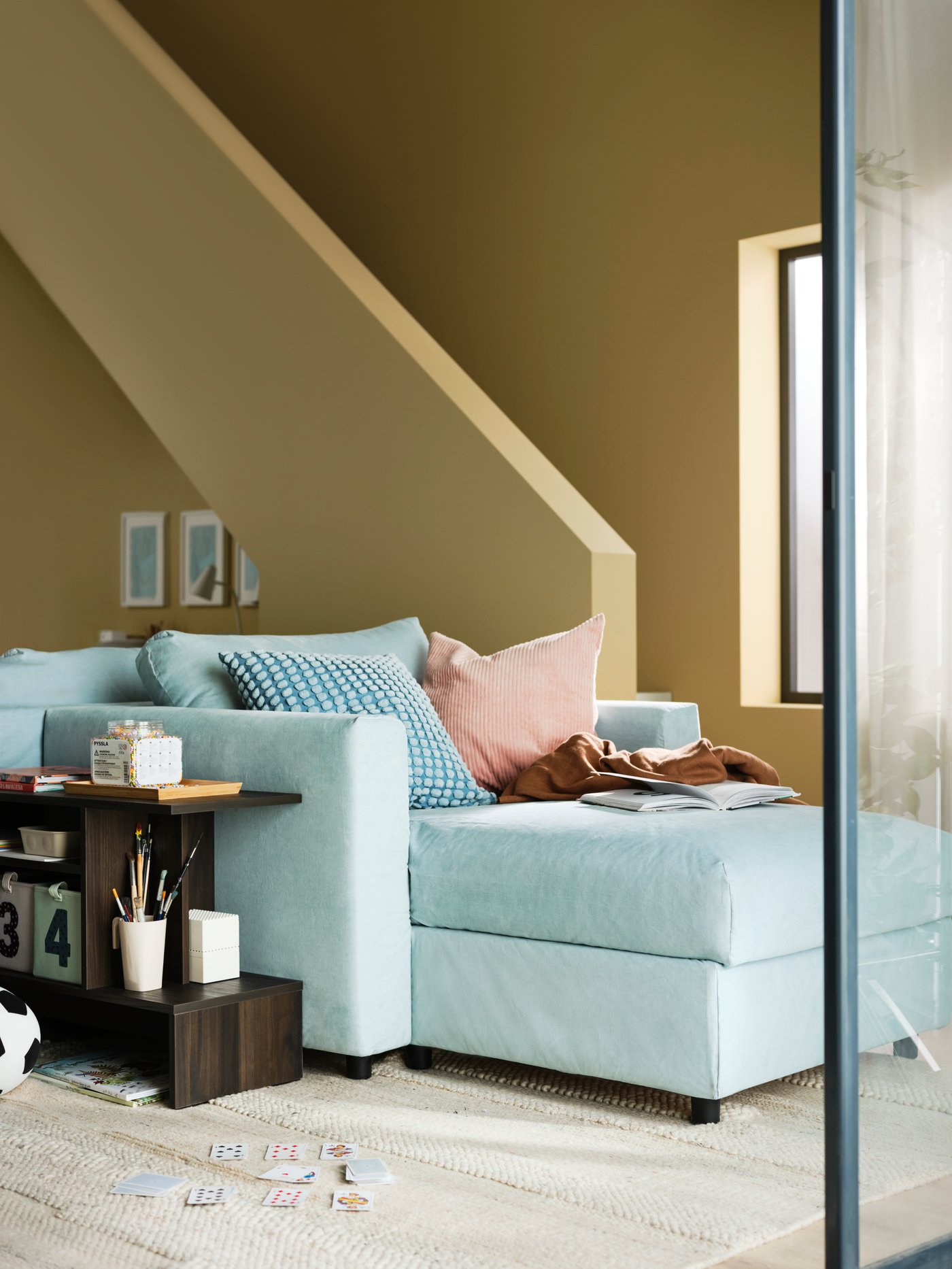 A light blue VIMLE chaise longue with cushions is in the middle of a living room with yellow walls close by a staircase.