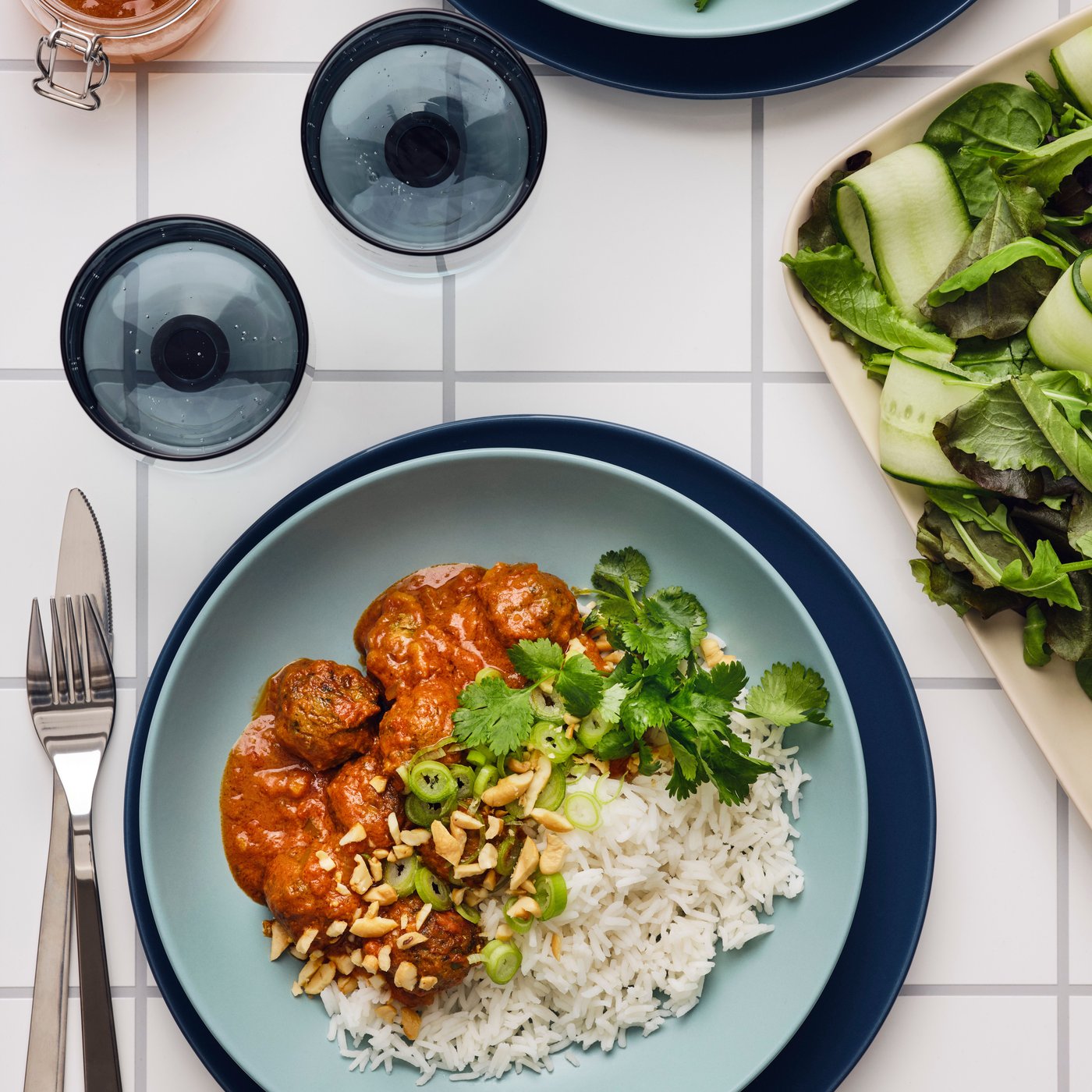 A turquoise plate is placed on top of a blue plate and contains rice and a stew and is garnished with coriander.