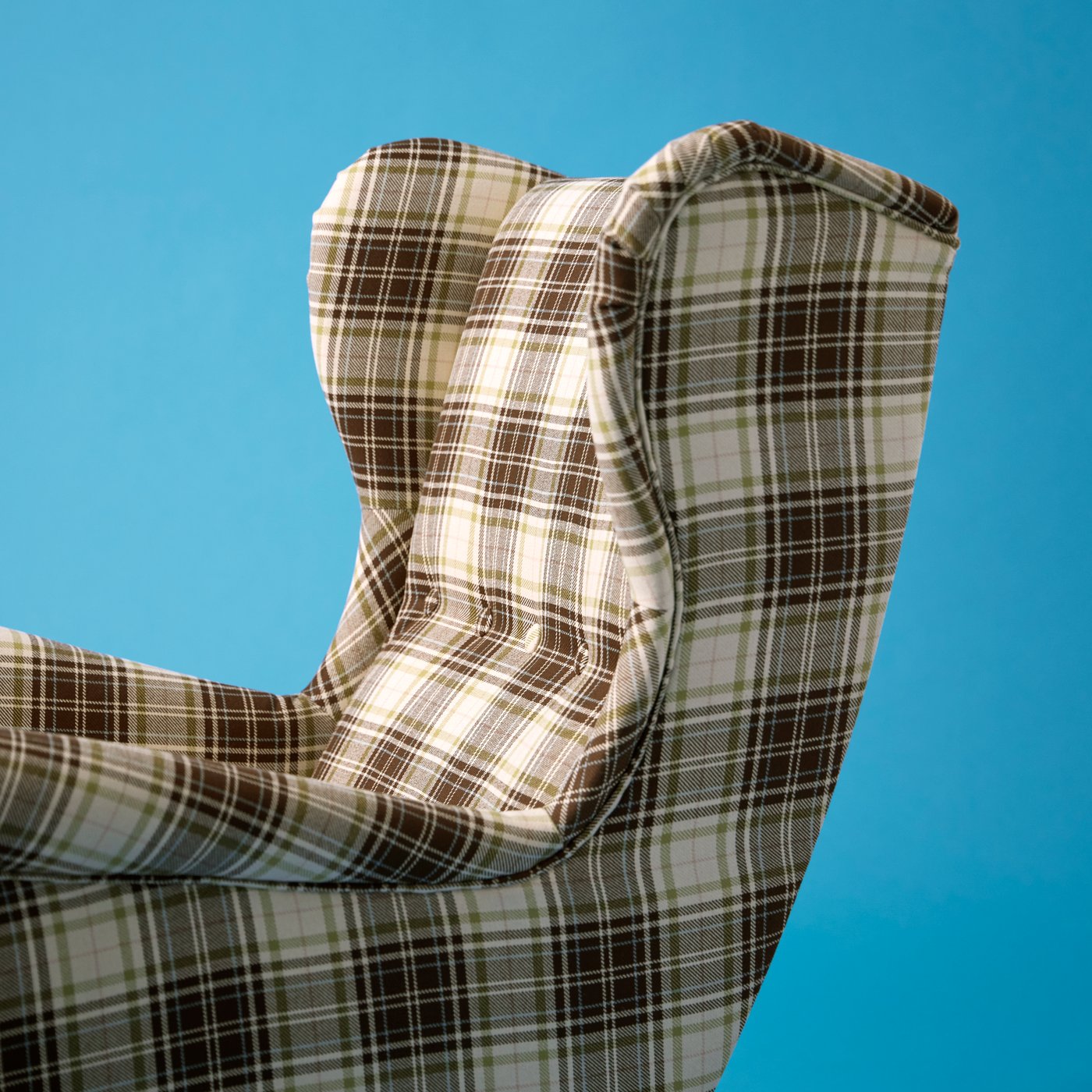 An empty STRANDMON wing chair in Talliden beige-brown, tartan-pattern fabric standing against a light-blue wall.