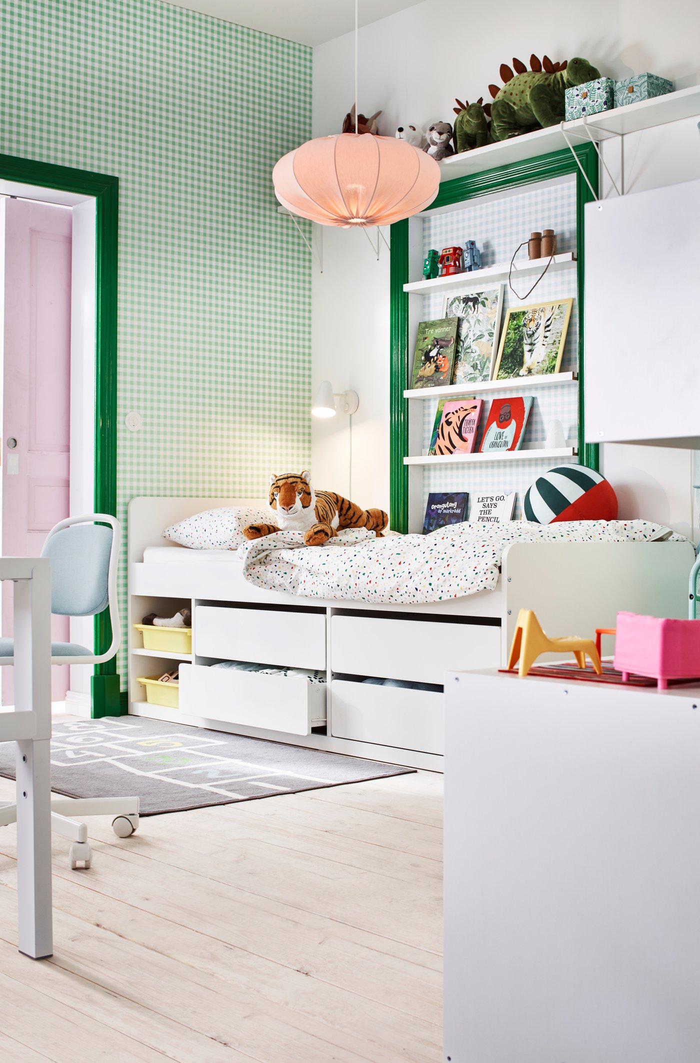 Teil eines Kinderzimmers mit grün-weissem Farbschema mit Büchern, Spielzeug und einem Bett mit mehreren Schubladen.