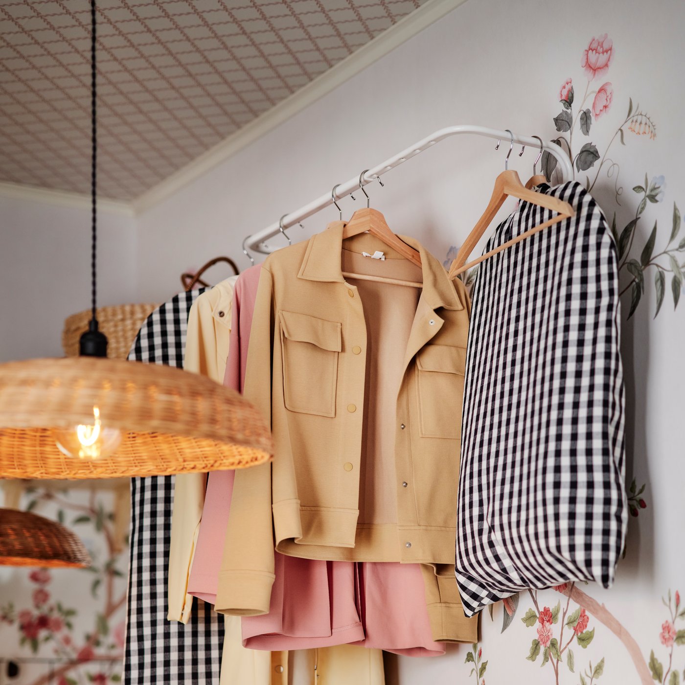 En vit MULIG klädstång högt upp på en blommig vägg håller olika jackor på BUMERANG galgar, varav några är täckta.