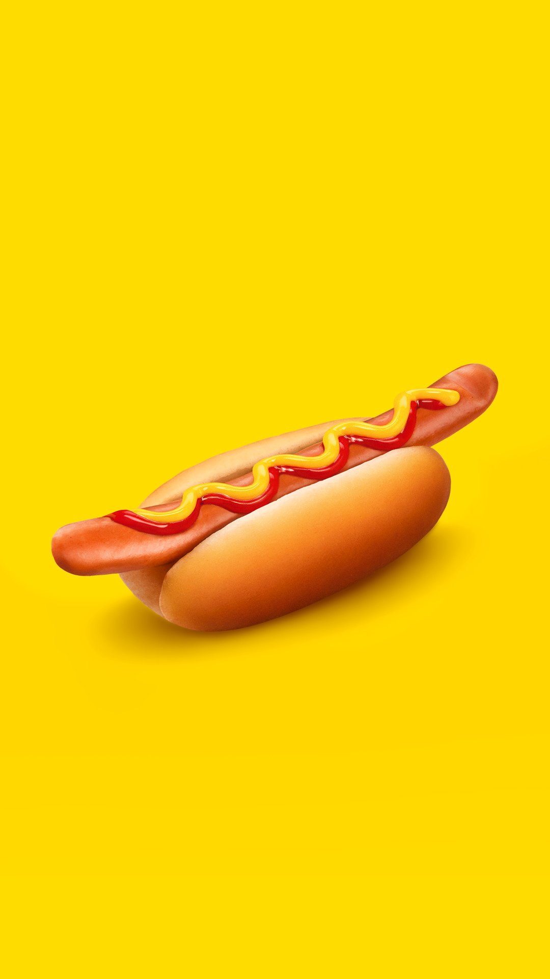 En klassisk varmkorv med bröd, ketchup och senap, mot en klar gul bakgrund.