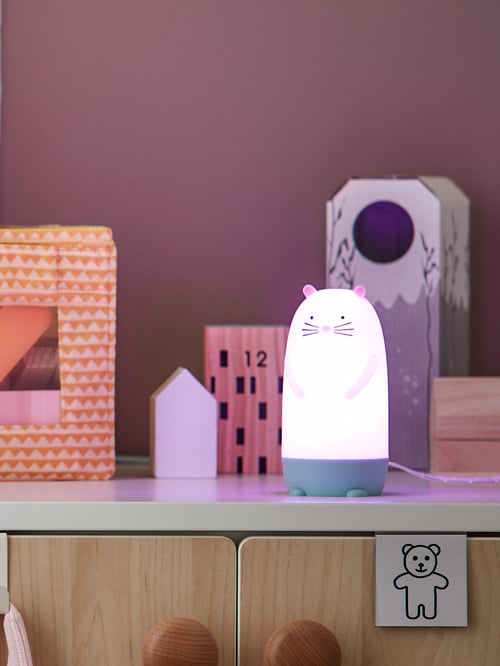 Camera pentru bebeluși și copii de aproape a unei lumini de noapte cu LED în formă de vidră multicoloră amplasată lângă o cutie dreptunghiulară.