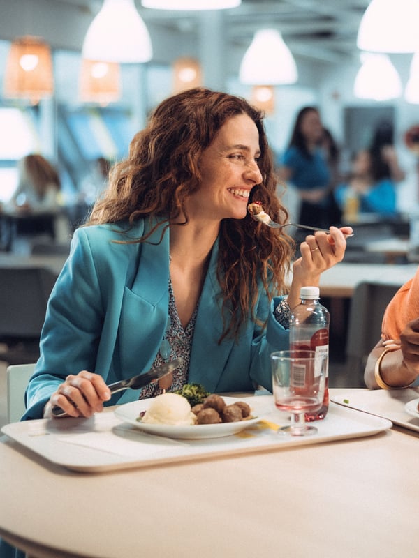 Eine Person sitzt in einem IKEA Restaurant, lacht und isst eine Mahlzeit.