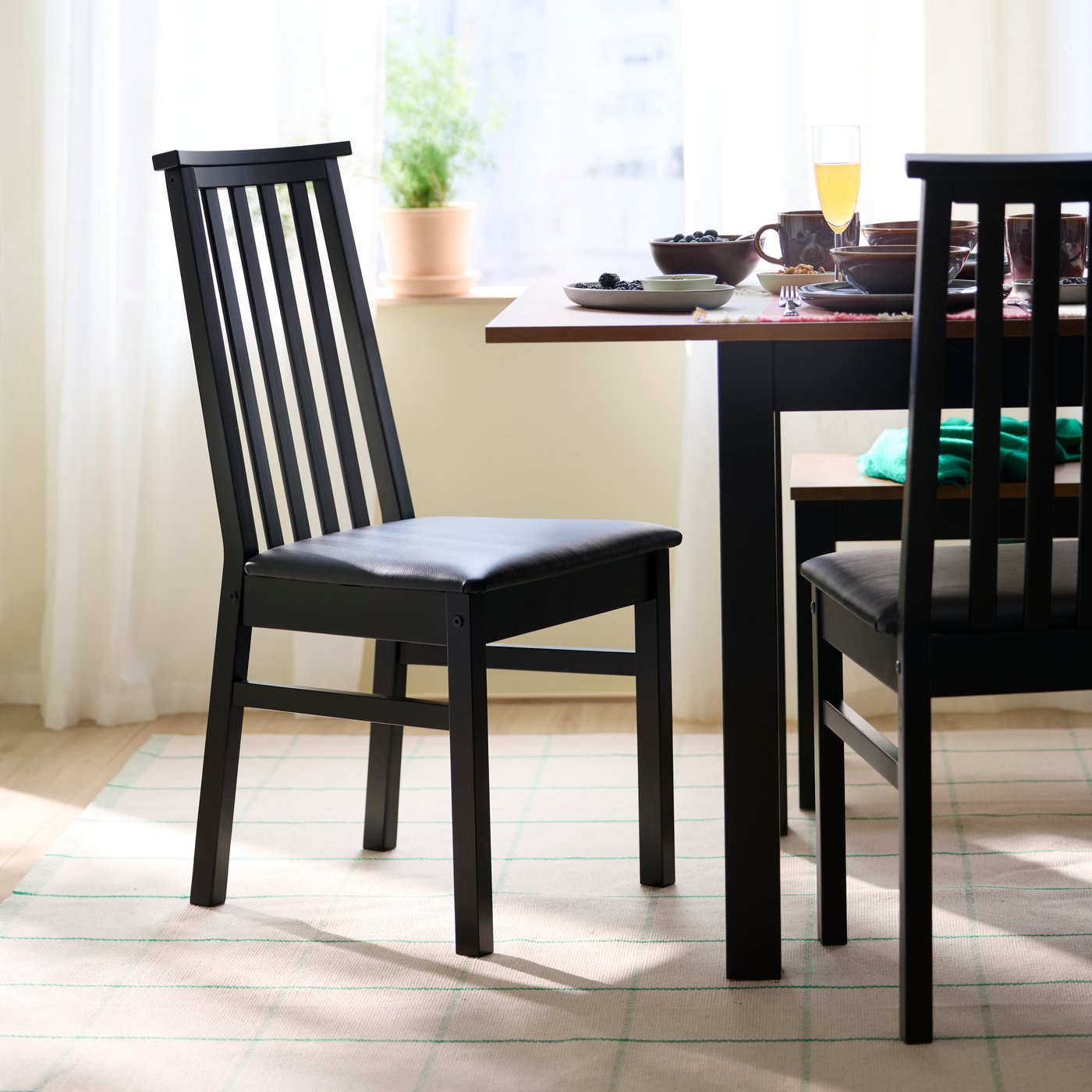 Deux chaises ÅLHULT noires avec siège rembourré au revêtement Bomstad noir sont placées à côté d’une table à abattants ÅLHULT noir/brun.