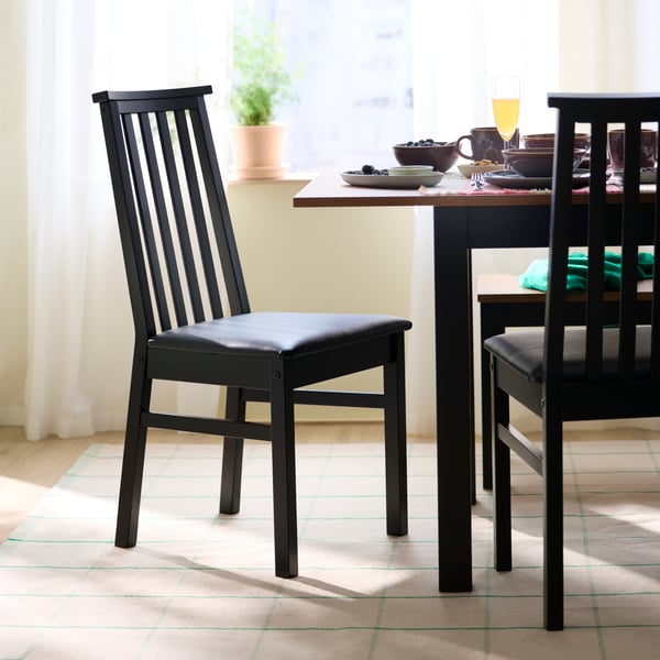 Deux chaises ÅLHULT en noir avec des sièges moelleux en noir Bomstad sont placées à côté d'une table extensible ÅLHULT en noir/marron.
