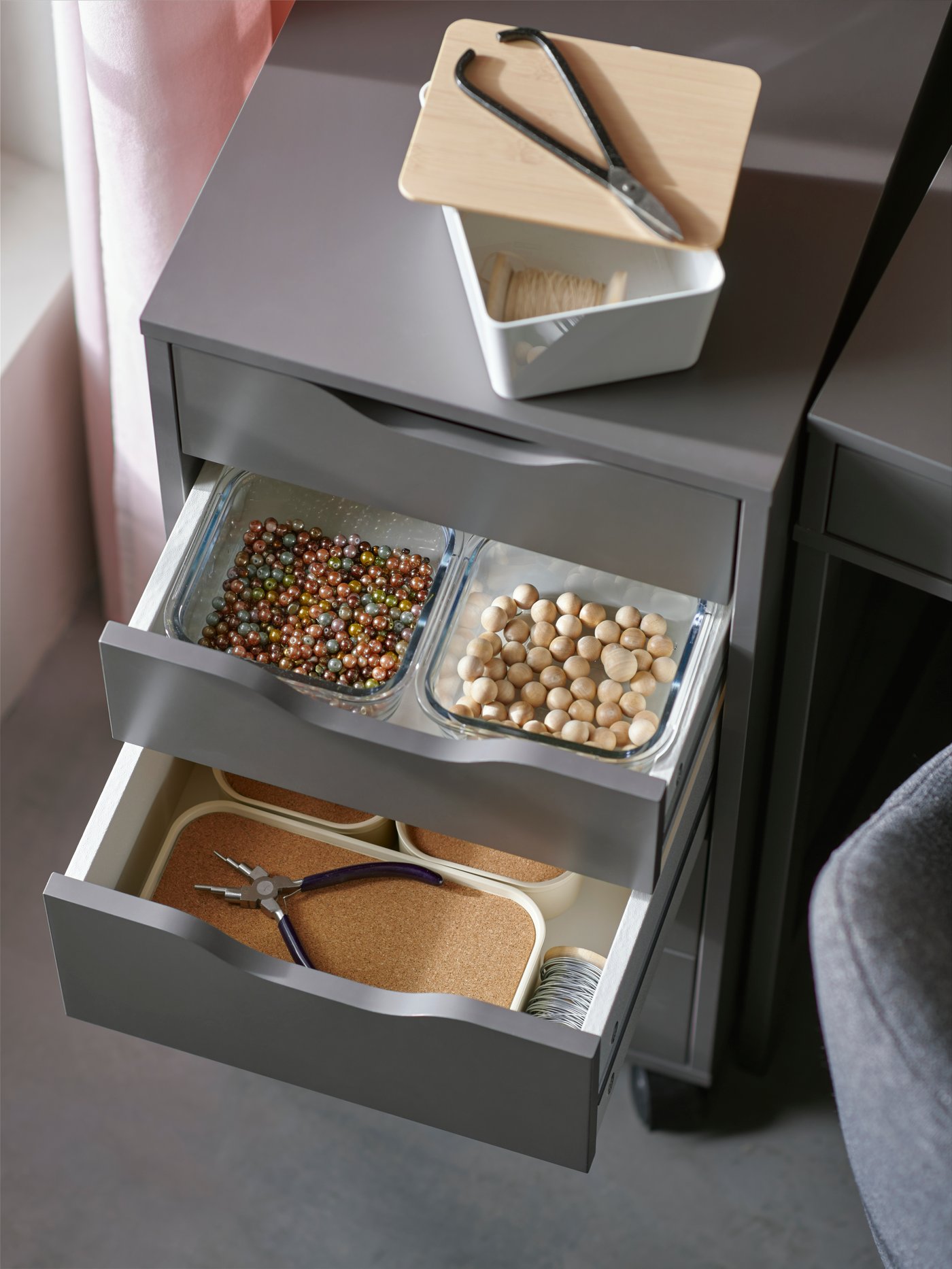 A dark grey ALEX drawer unit with open drawers with hobby supplies that are organised with containers in different sizes.